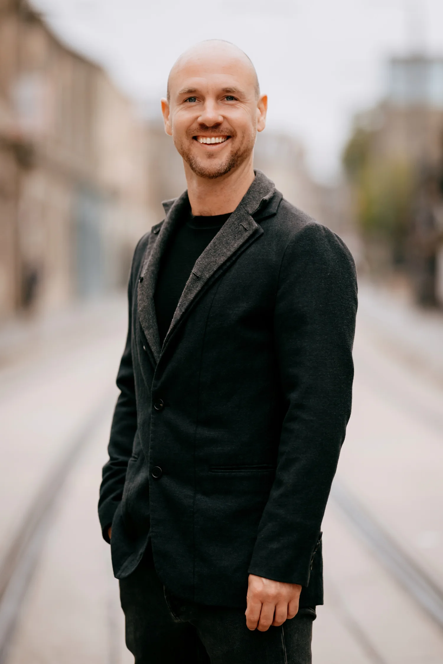 Paul Holmes smiling outdoors in a dark blazer.